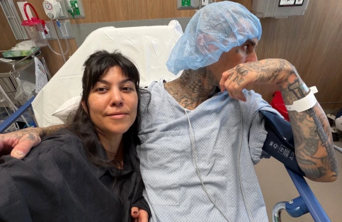Kourtney Kardashian smiling next to Travis Barker as he lay in a hospital bed / © Instagram